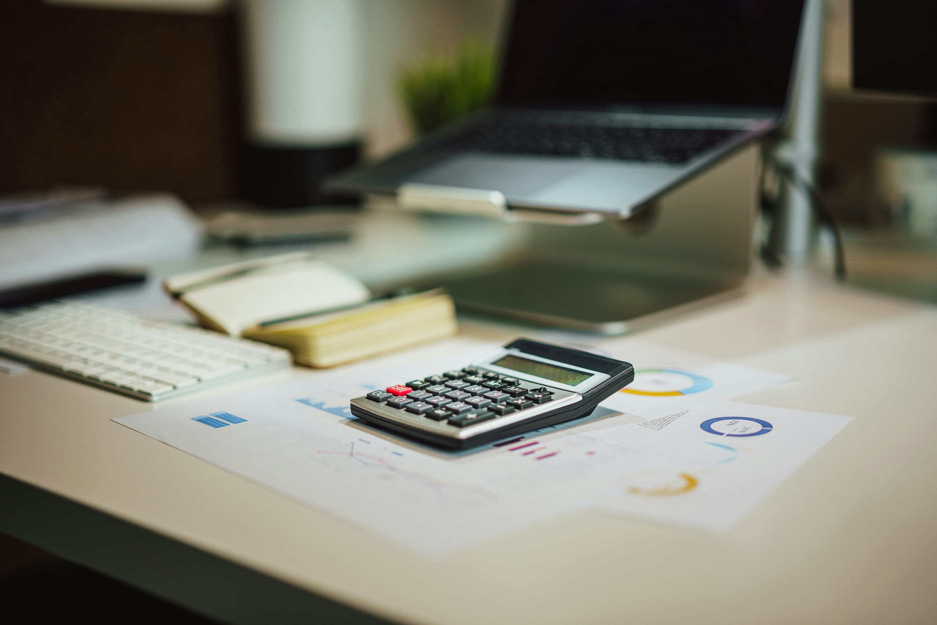 Calculator and financial reports on a desk next to a laptop